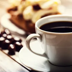 En kopp kaffe på en tallerken med småkaker i bakgrunnen