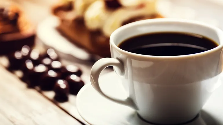 A cup of coffee on a saucer with cookies in the background