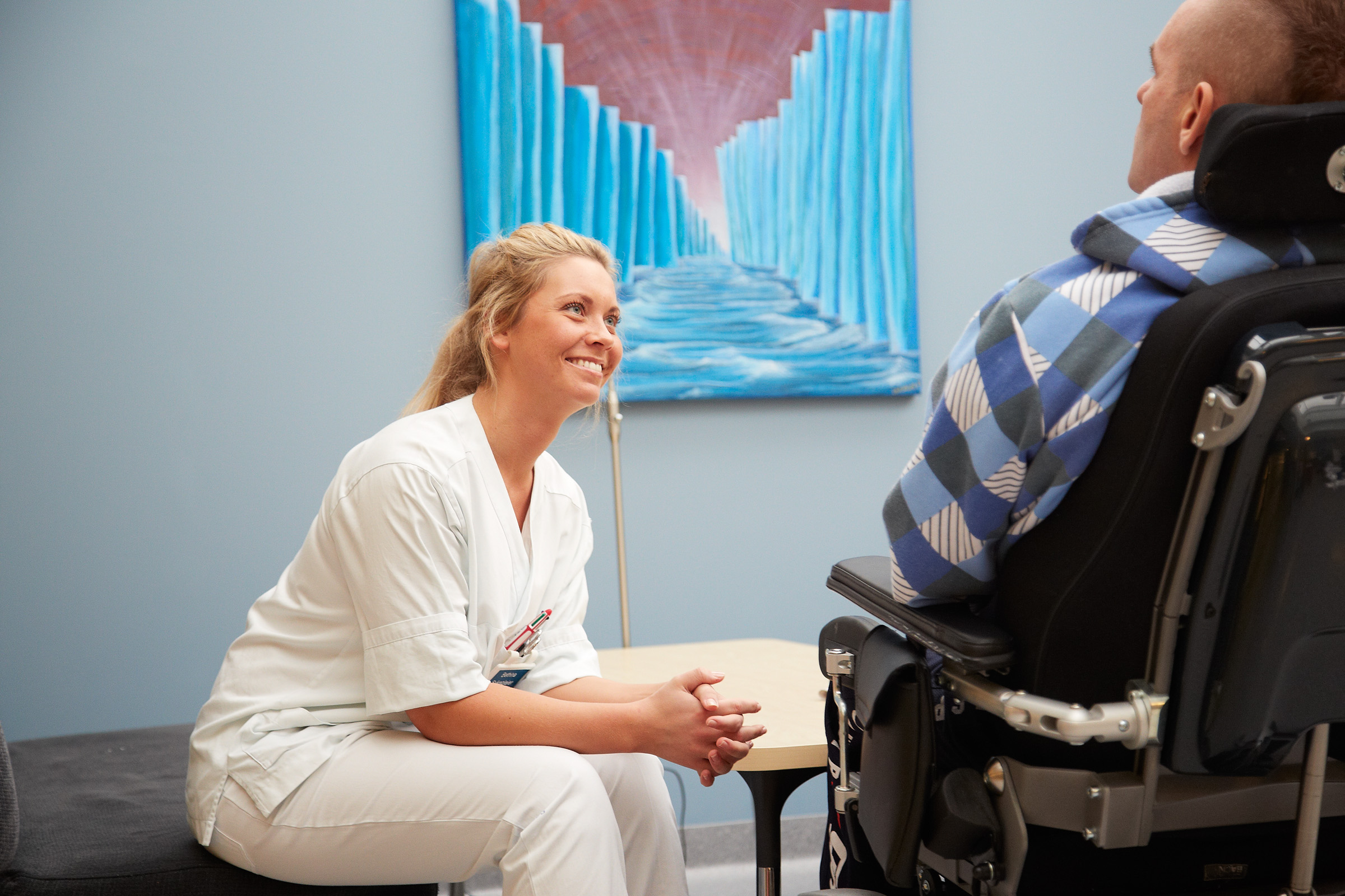 En helsearbeider som snakker med en mann i rullestol.