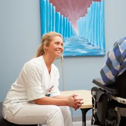 En helsearbeider som snakker med en mann i rullestol.