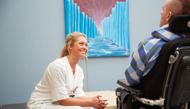 En helsearbeider som snakker med en mann i rullestol.