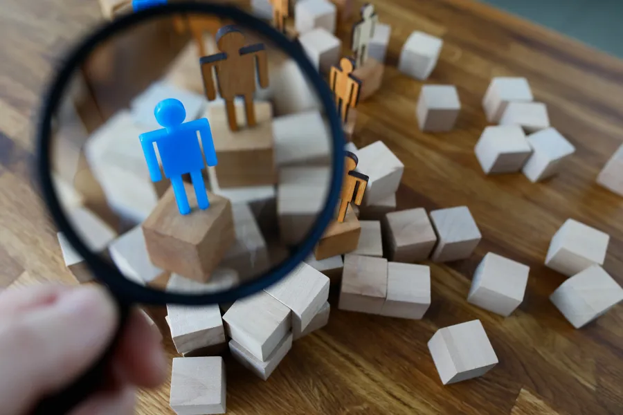 menneskefigurer i tre. En er blå, fremheves med forstørrelsesglass.