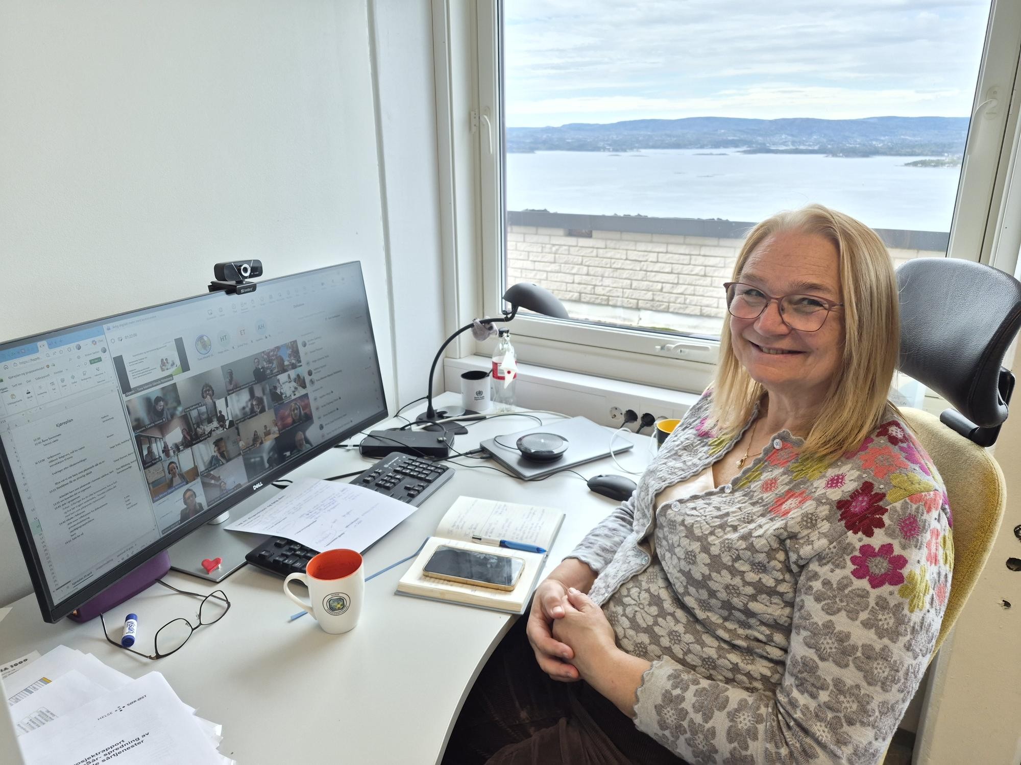 En person som sitter ved et skrivebord med en datamaskin og et vindu
