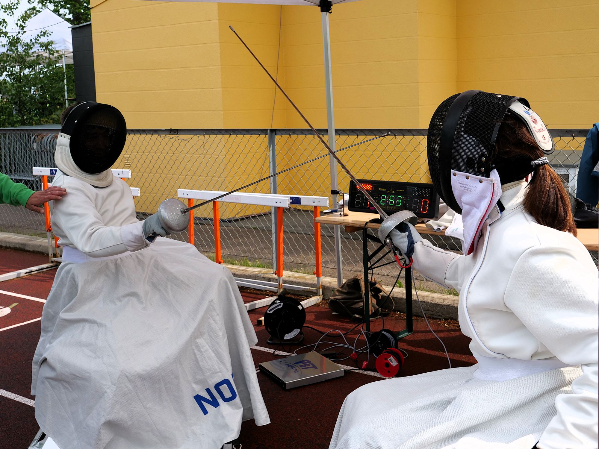 To sittende personer fekter iført fekteutstyr.