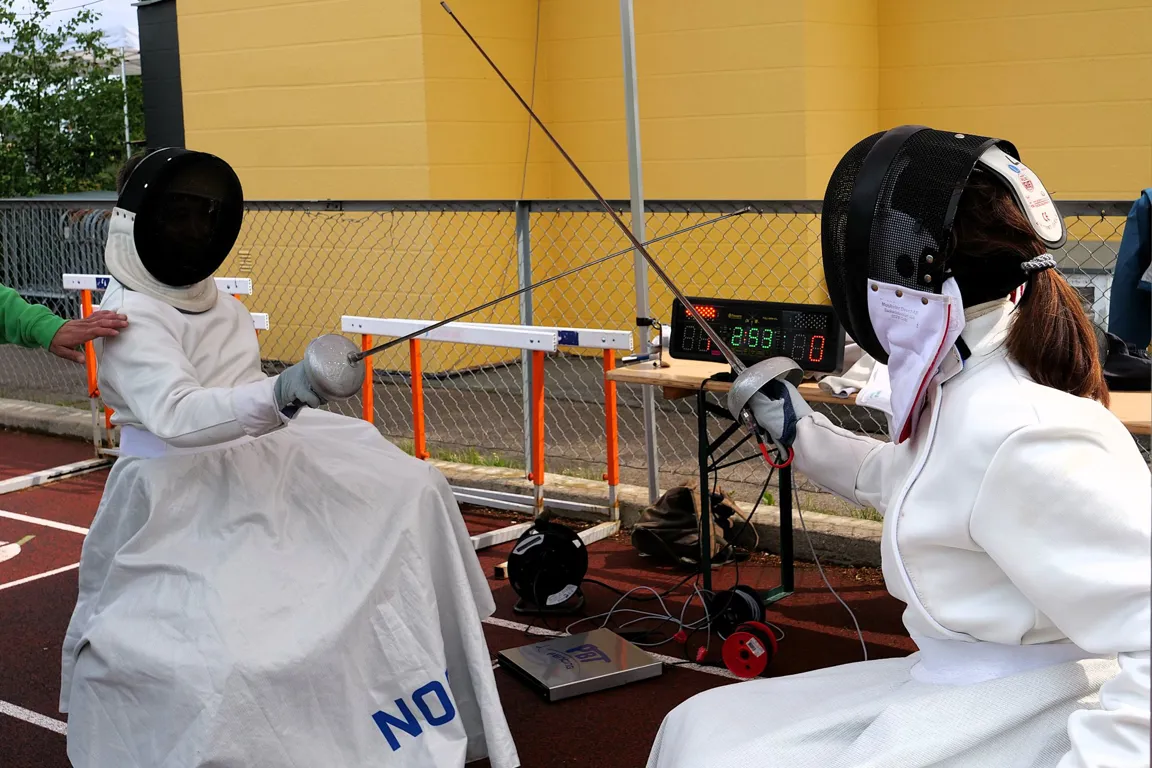 To sittende personer fekter iført fekteutstyr.