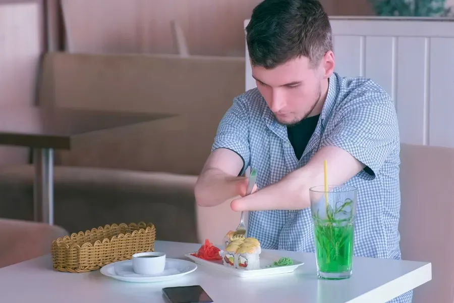 Ung mann med armdysmeli spiser sushi