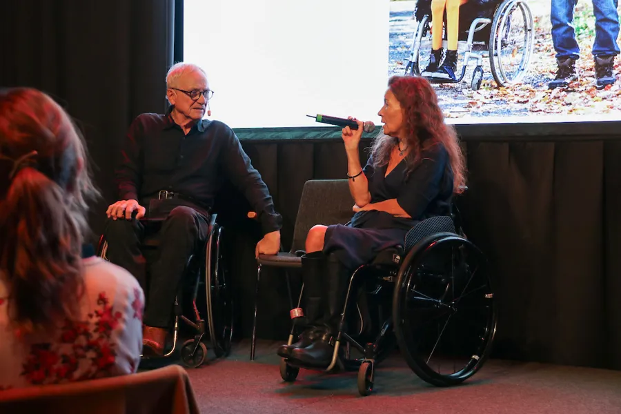 A man and a woman sitting in a wheelchair on a stage