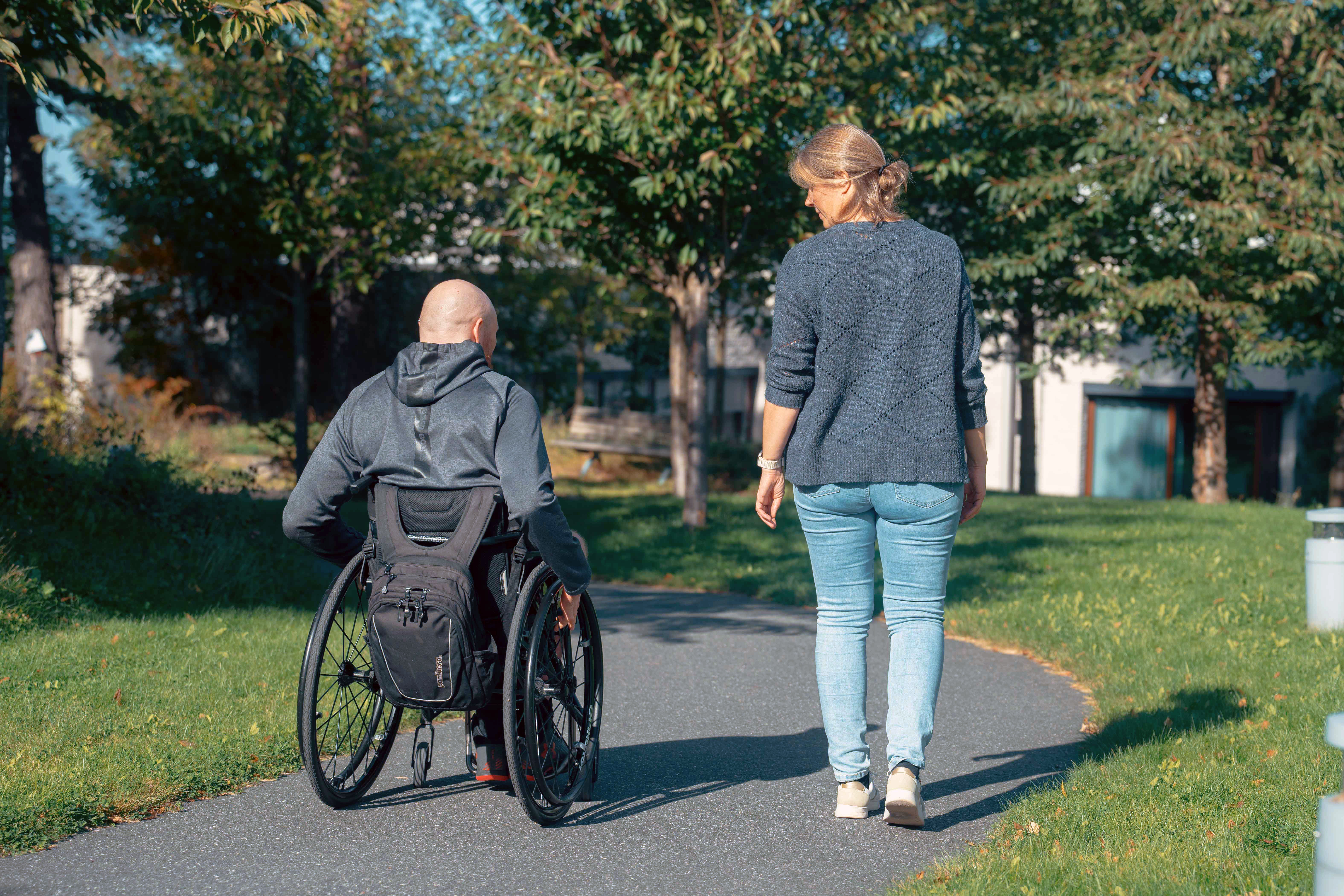 En mann i rullestol og en kvinne som på tur i en park