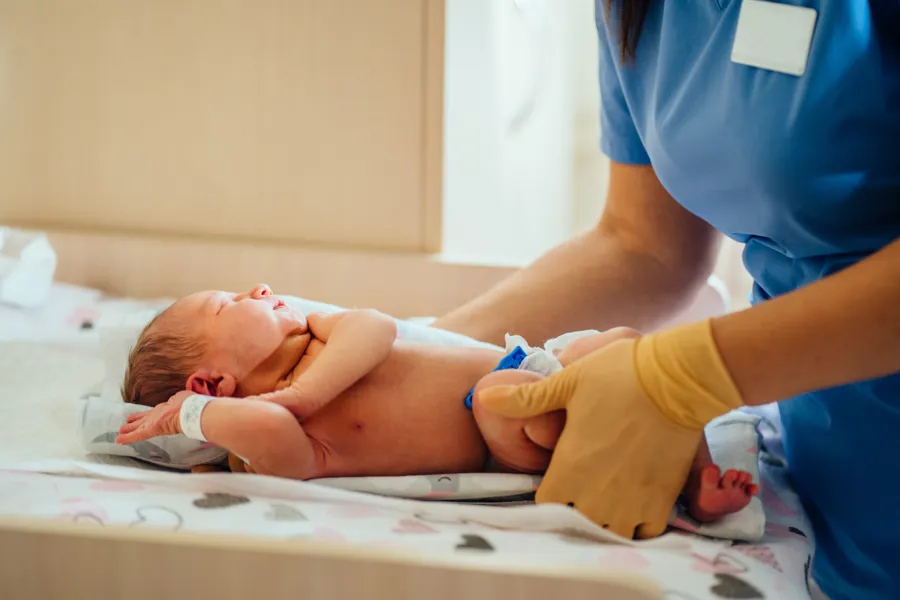 Nyfødt baby ligger på stellebord og helsepersonell håndterer den.