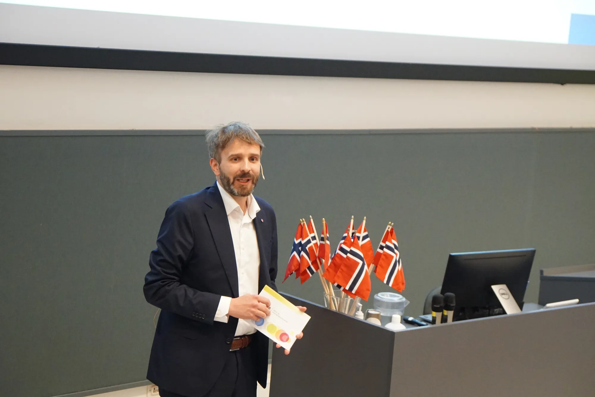 Helseminister Vestre står på en talerstol. Han holder i talekort. Norske flagg bak han