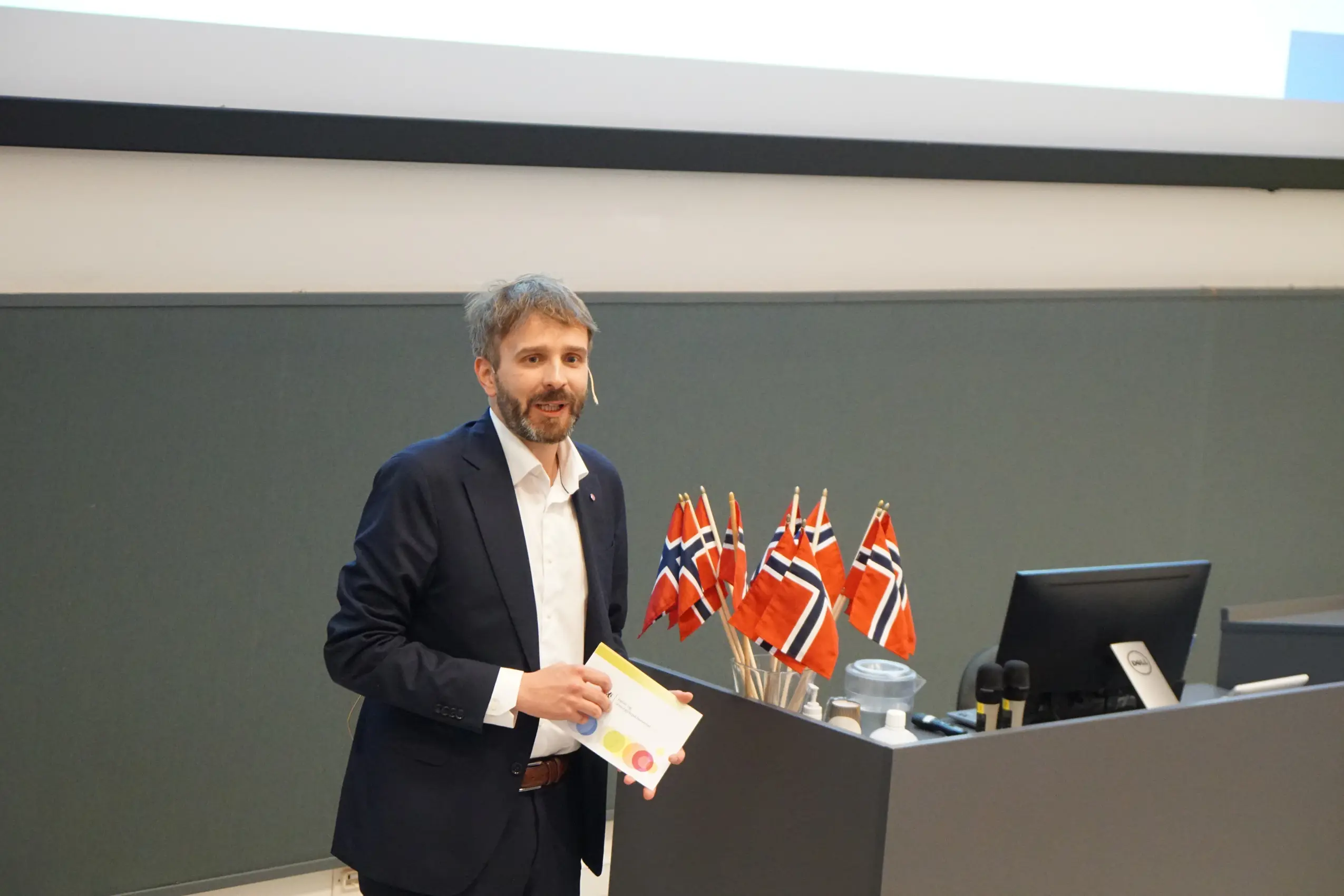 Helseminister Vestre står på en talerstol. Han holder i talekort. Norske flagg bak han
