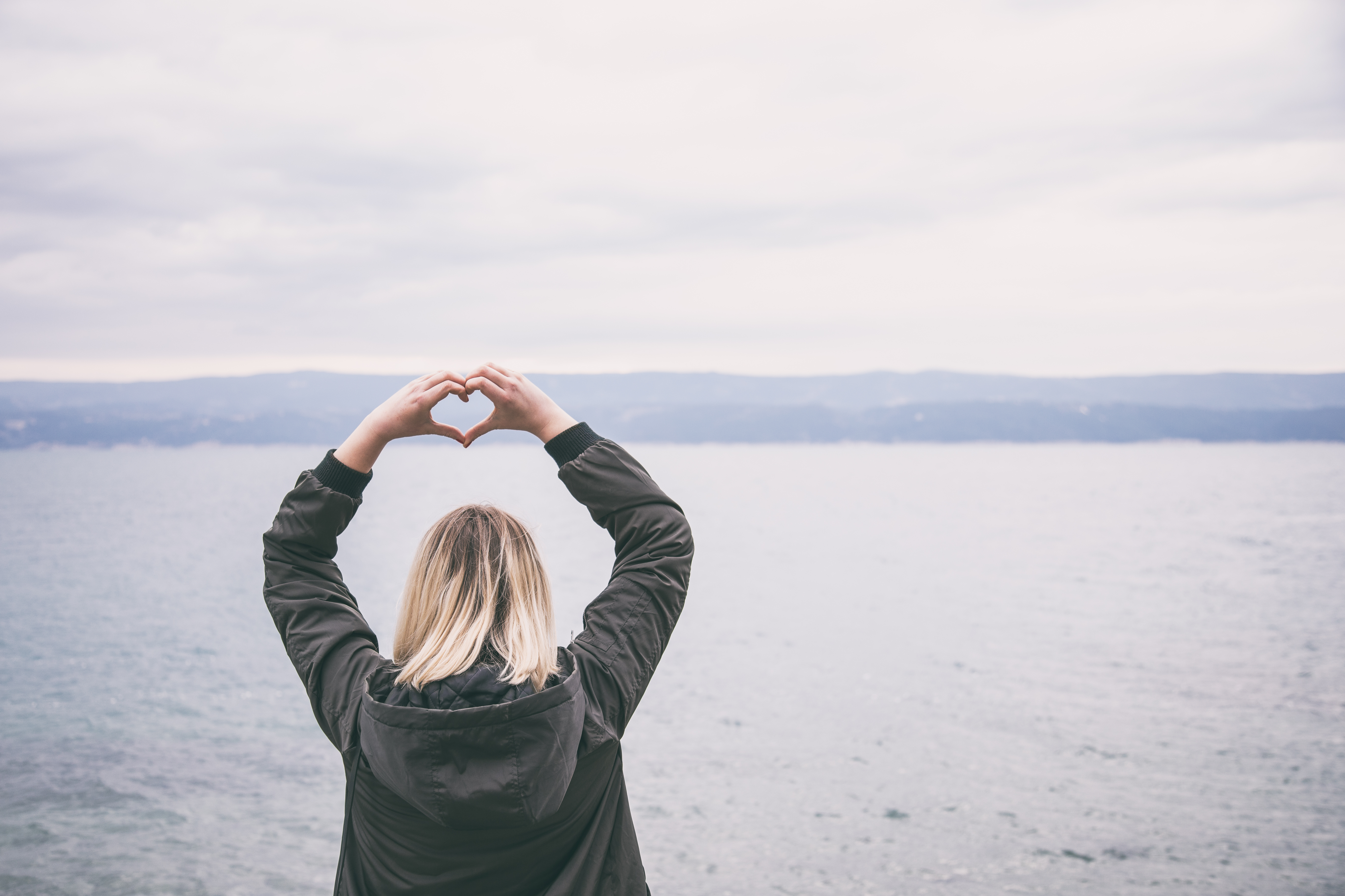 Bilde av dame som ser utover havet og holder hendene som et hjerte