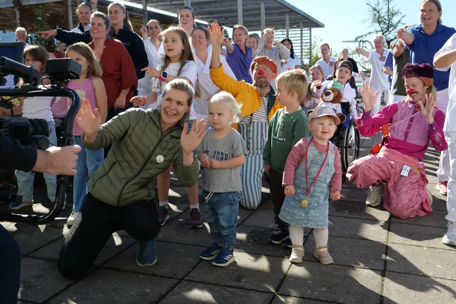 Barn, voksne og sykehusklovner danser Bli med-dansen på en takterrasse