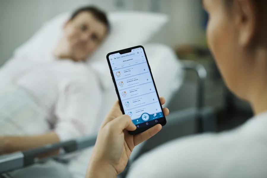 Kliniker holder mobiltelefon i hånden ved pasientseng
