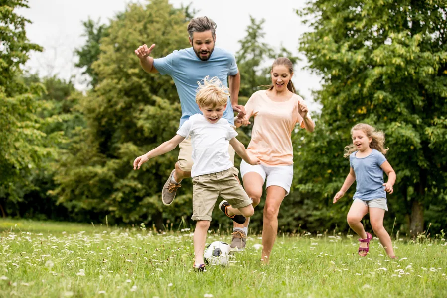 Bilde av foreldre og to barn som sparker fotball i gresset