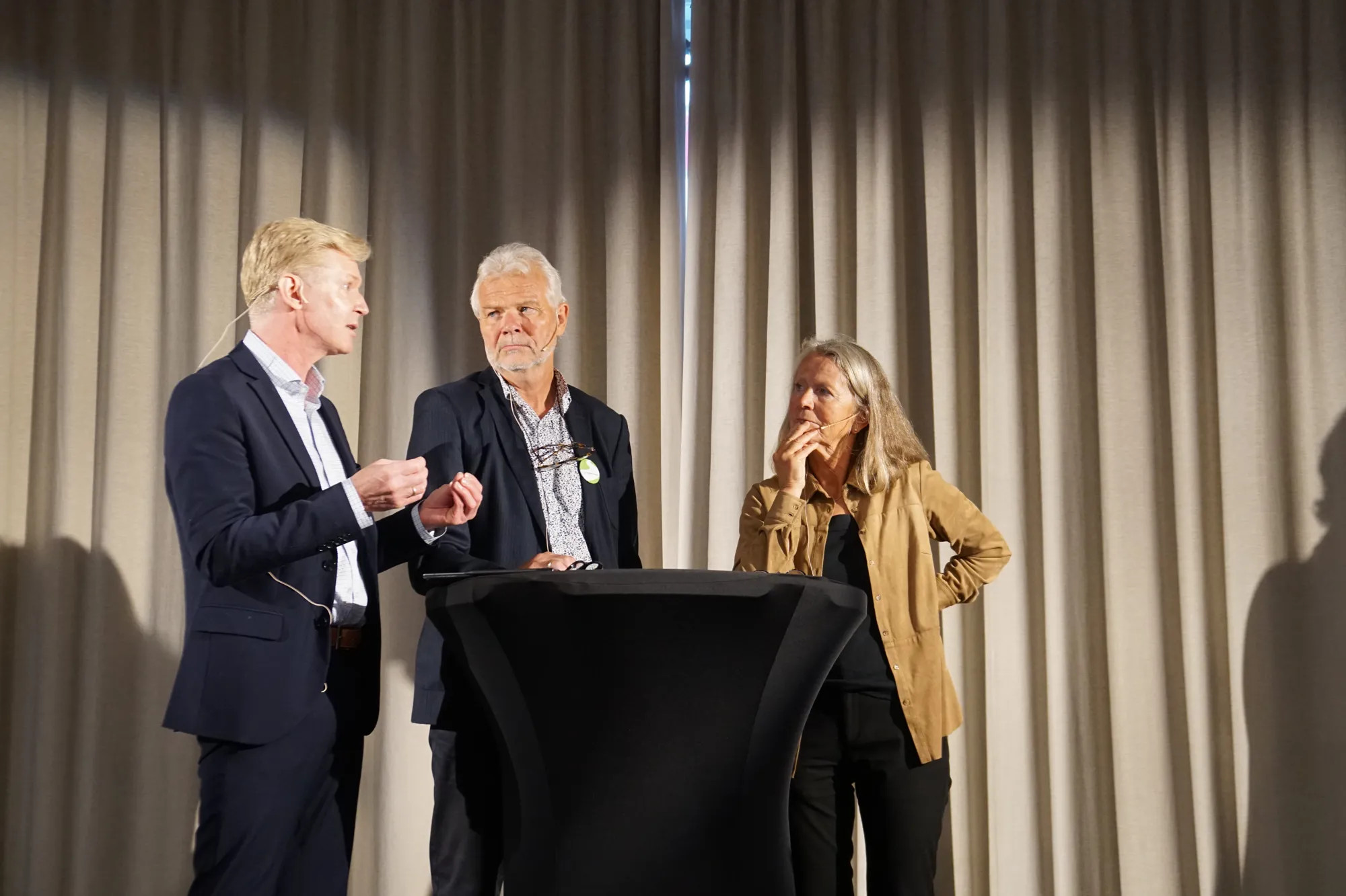 To menn og en kvinne i samtale på en scene