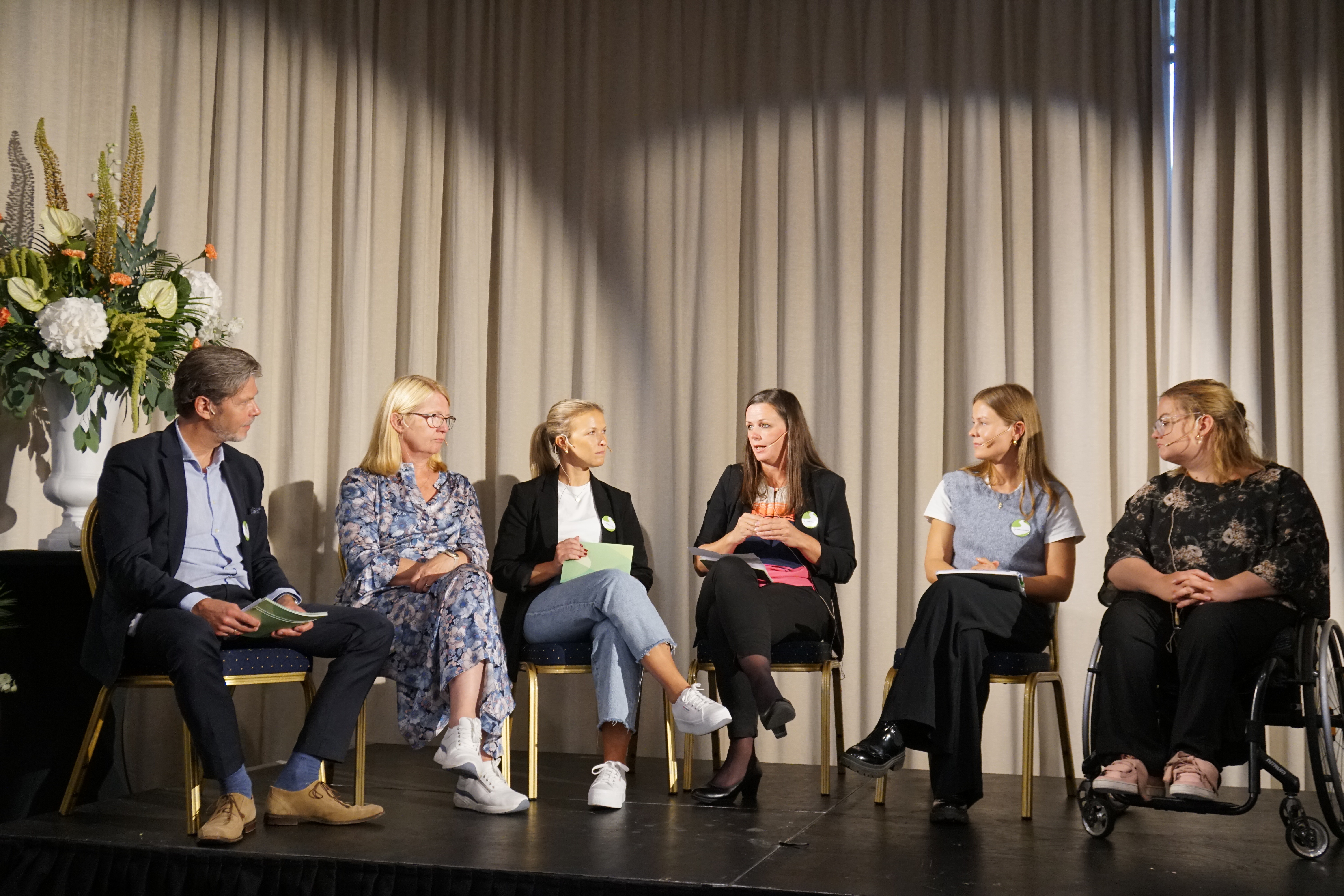 Seks personer sitter på en scenen og snakker sammen