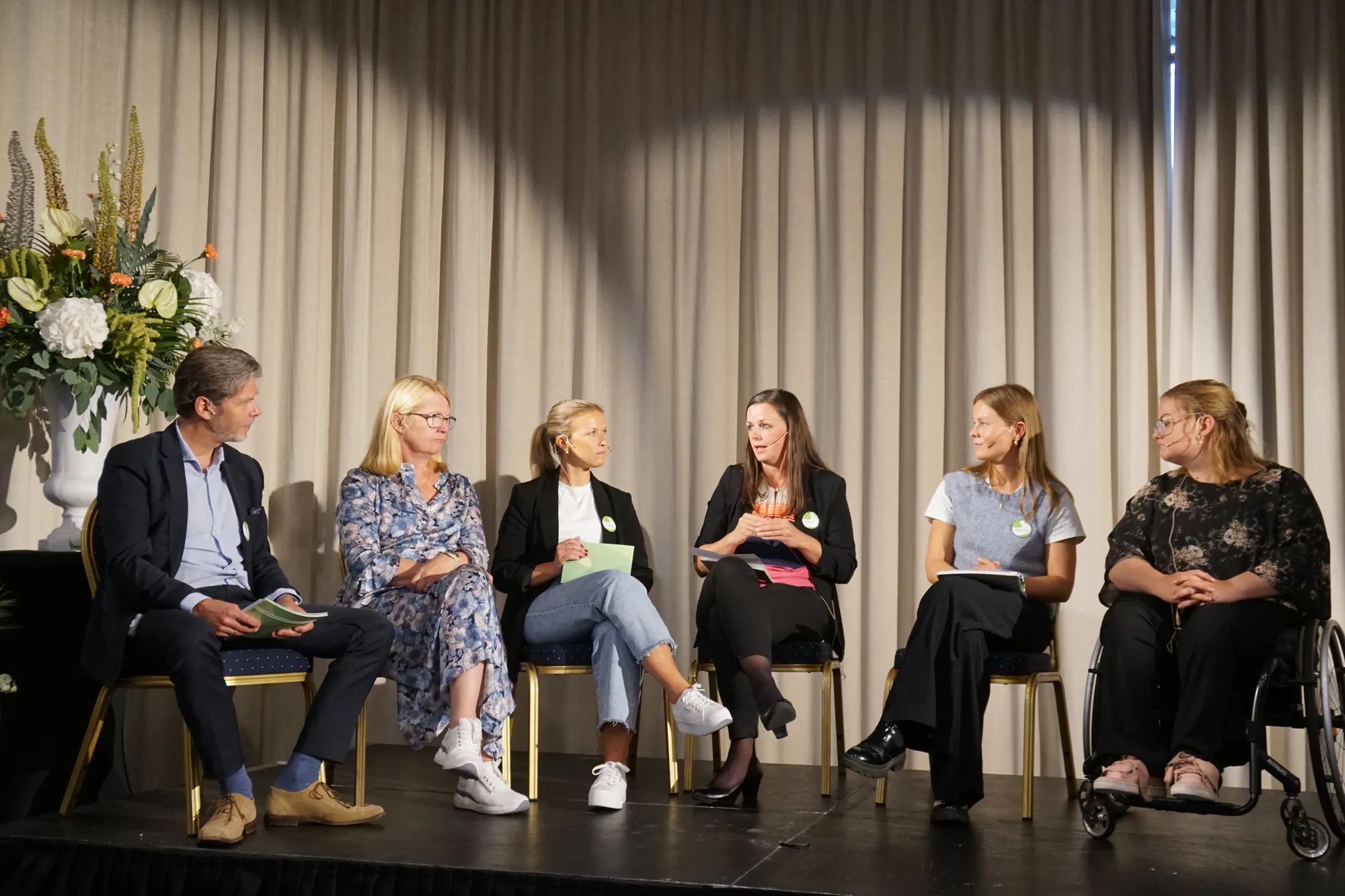 Seks personer sitter på en scenen og snakker sammen