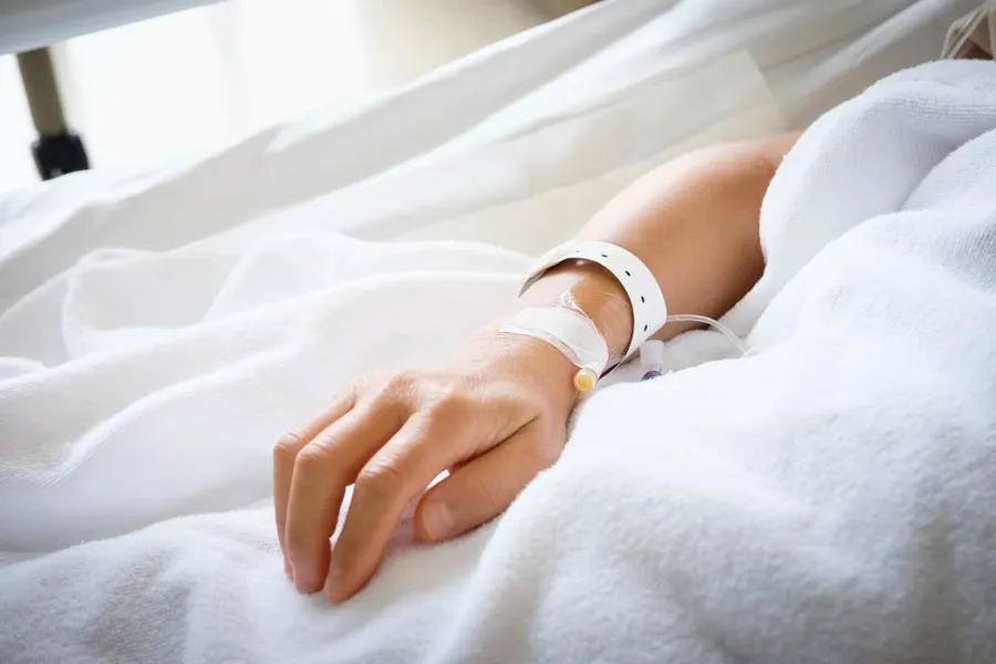 Nærbilde av hånd til pasient som ligger i sykehusseng med intravenøs i hånden.