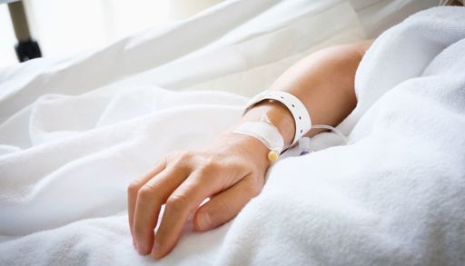 Nærbilde av hånd til pasient som ligger i sykehusseng med intravenøs i hånden.