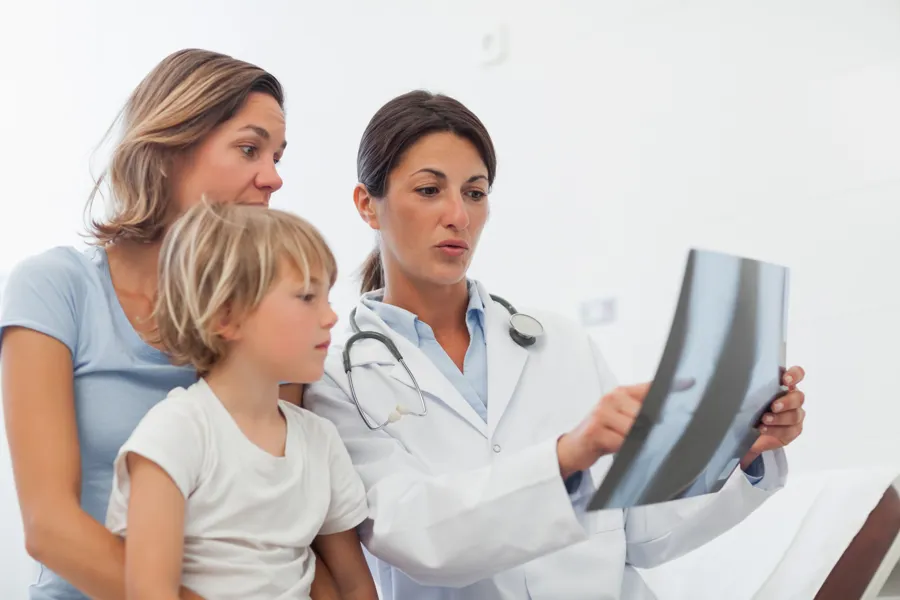 Lege som ser på et røntgenbilde sammen med mor og barn