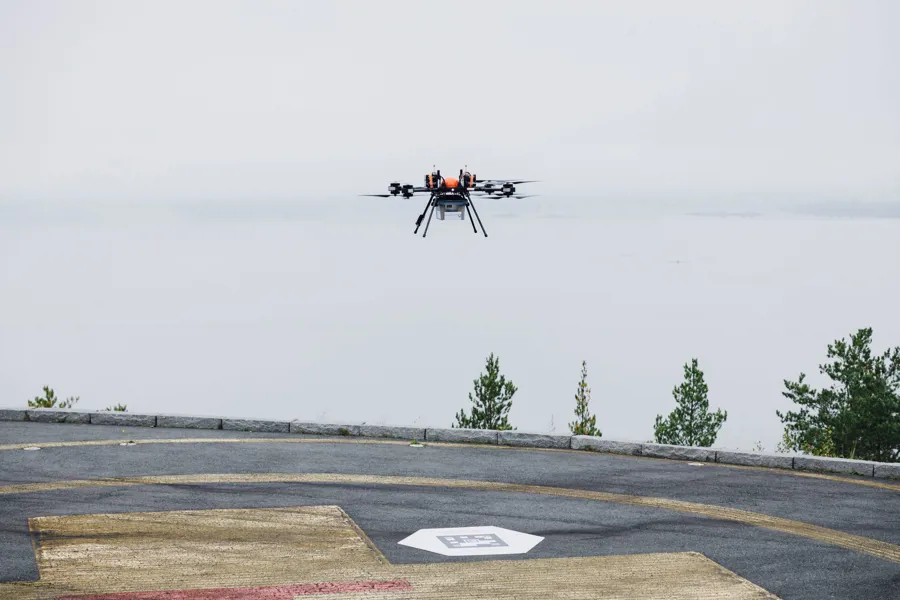 Drone flyr over helikopterplass med boks med blodprøver under seg