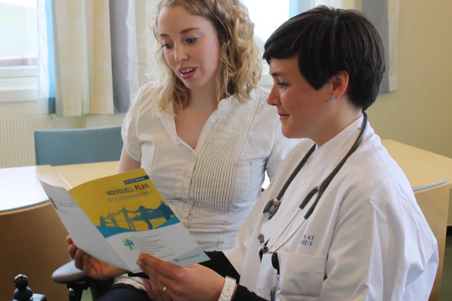 En lege som viser en pasient noe på boken