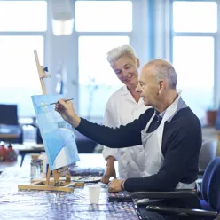 En mann som maler et bilde. En ergoterapeut ser på.