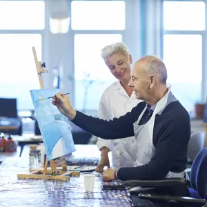 En mann som maler et bilde. En ergoterapeut ser på.