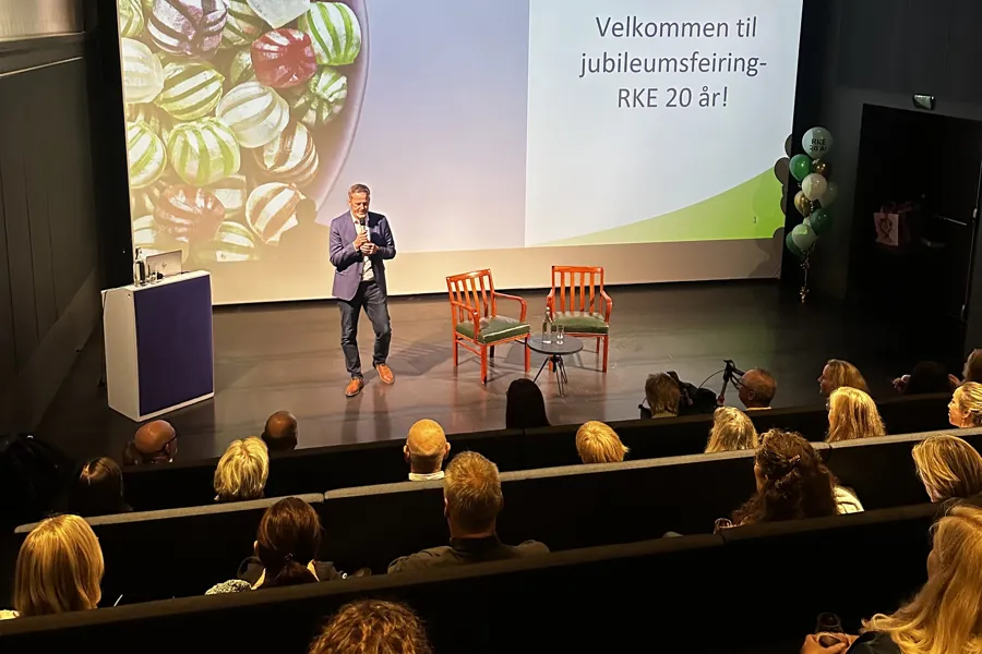 En person som står på en scene med en gruppe mennesker som sitter i stoler