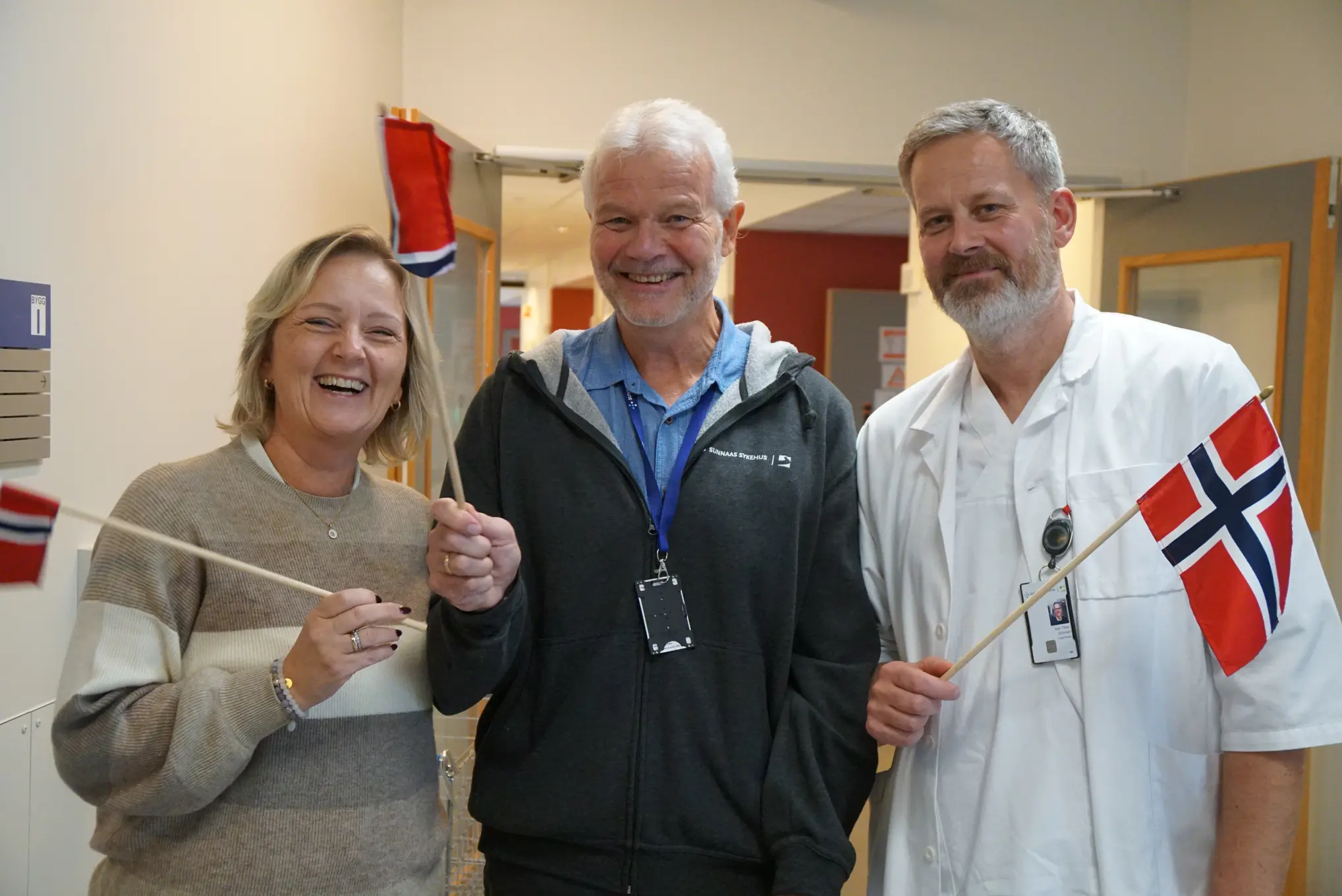 En kvinne og to menn smilende med Norske flagg
