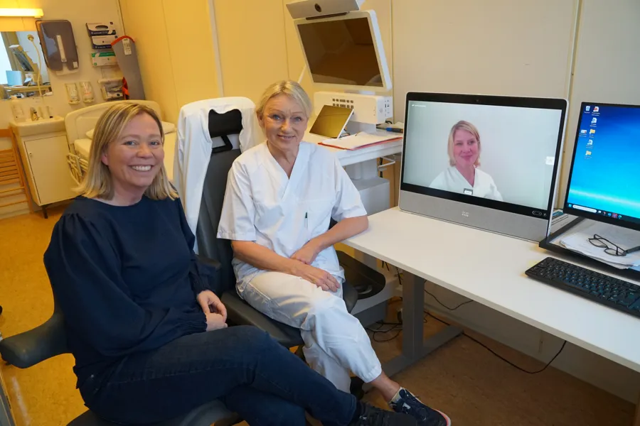 To kvinner sitter ved et skrivebord, en tredje kvinne er med i videokonferanse på pc-skjermen på pulten