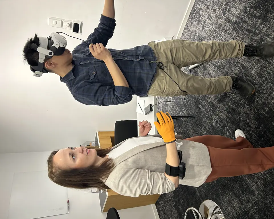 Anne-Marthe Sanders tester en hanske med digitale sensorer. Ved siden av henne står en forsker fra Singapore og tester VR-briller
