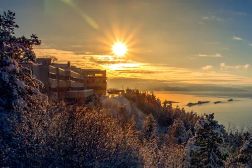 En bygning på en høyde ved vannet med solen i bakgrunnen