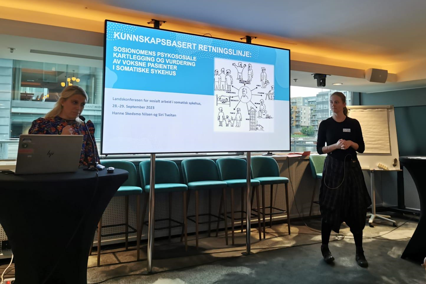 En kvinne som står ved siden av en mann som sitter ved et bord med en bærbar datamaskin